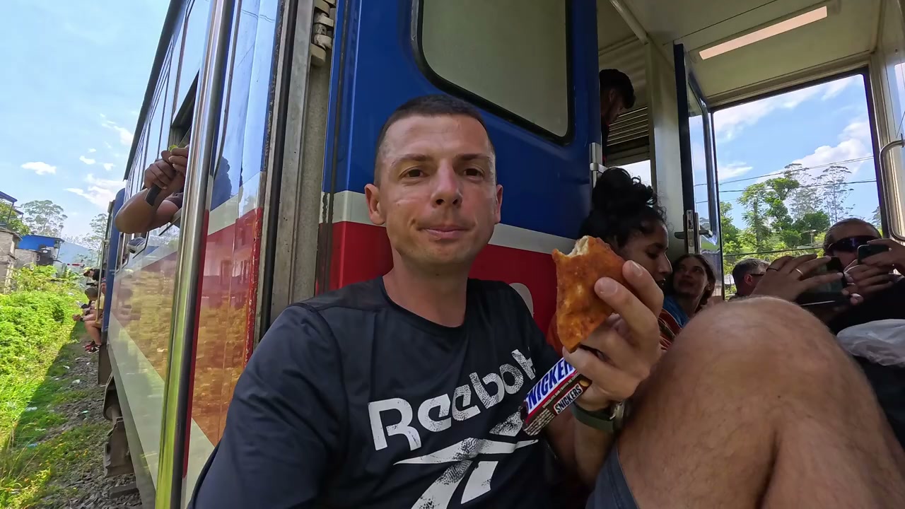 Traveler sitting in the open door of the moving Kandy to Ella train
